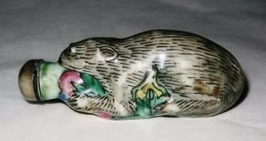 GLAZED PORCELAIN SQUIRREL SNUFF BOTTLE c This glazed porcelain snuff bottle is crafted in the shape of a squirrel holding onto a fruit. Made some time between 1796 and 1840, the mouth opening is fitted with a stopper.