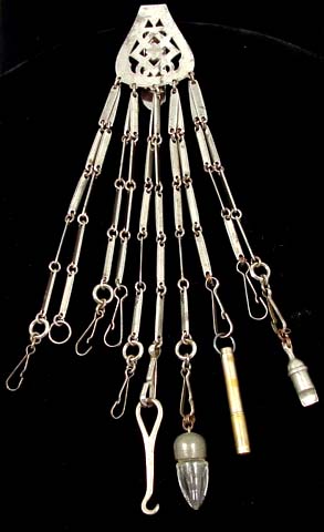 1890ca In 1871 the fashion of wearing châtelaines was revived by Princess Alexander of Wales, who wore one. They remained in vogue for another 20 years. Worn by housewives or housekeepers, the numerous chains carried a wide range of useful objects. This châtelaine is made of cut steel with a deep hook, which attached over the woman's waistband. The remaining tools include a shoe hook, whistle, needle case and small perfume bottle. Circa 1890.