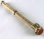 Chatelaine Retractable Pencil With Inset Carnelian Stone A mechanical pencil with an ornate design and the top screw off cap. The top has an inset Carnelian Stone and below it is a hoop that slides for a Châtelaine. Circa 1893.