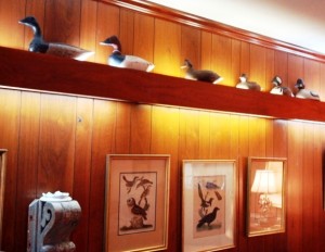 blogdecoydecor4 Many decoys “swimming” on a light bar in a paneled living room make an effective display. The light bar uses fluorescent bulbs that burn cool and the lights are not on long so the decoys are not affected by undue heat. Decoys include a New Jersey Brandt, Maryland Canvasback, H.V. Shourds female Scaup, and a pair of modern Buffleheads by Charles Crookes. Engravings by Wilson hang on the wall below.