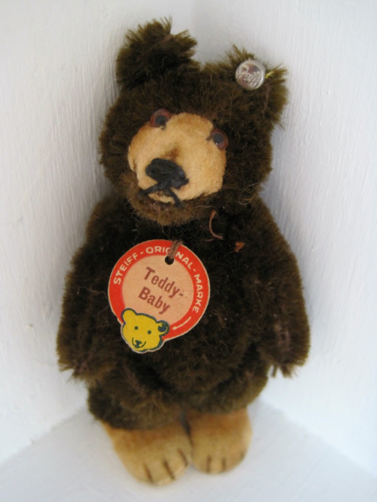 teddybaby1 This precious 9-cm Teddy Baby is from my personal collection; he is five ways jointed, deep chocolate brown, and has his signature tan velvet muzzle with a closed mouth and flat, broad feet. The 9-cm did not have the red leather collar. He is in pristine condition with his Steiff “raised script button” or RSB, crisp chest tag, and even his white linen “US Zone” tag stitched into his back seam. He dates from the very early 1950s.