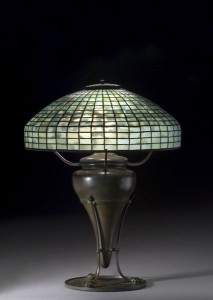 TIFFANY STUDIOS GEOMETRIC LEADED GLASS TABLE LAMP This 18-inch leaded glass geometric shade in blue-green mottled glass, supported by a rare Tiffany bronze base of urn form with paw feet on flat disk, sold for $17,825 (including the buyer’s premium) in an October 2006 auction.