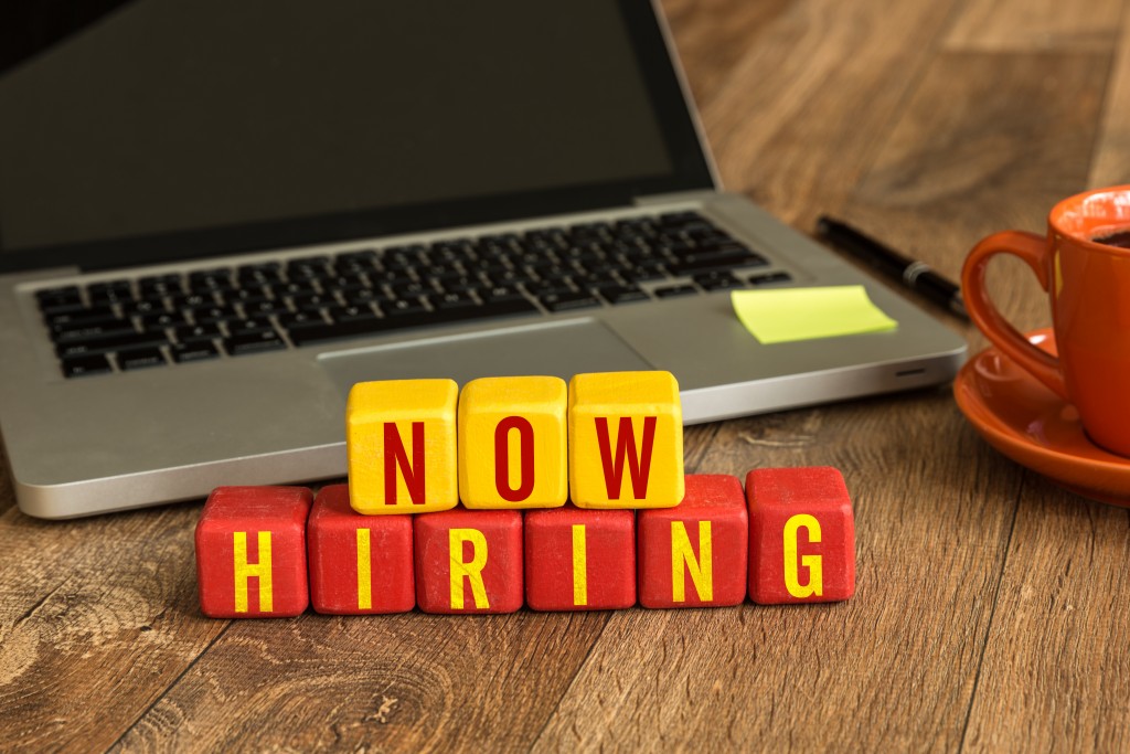 Now Hiring written on a wooden cube in a office desk